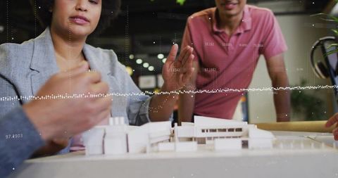 Architects collaborating over scale model with digital data overlay for urban planning