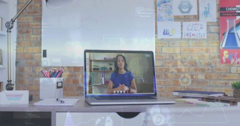 Remote teacher delivering virtual lesson on laptop at home desk with exposed brick wall