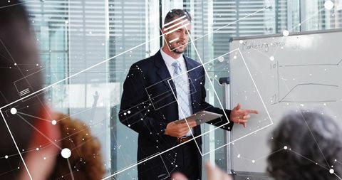 Presenting Executive Pointing at Whiteboard Holding Tablet in Boardroom with Data Overlay