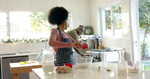 Couple baking together in sunlit modern kitchen pouring batter into glass bowl