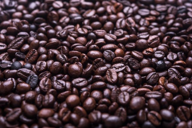 Close-up view of roasted coffee beans creating a rich, textured background. This image is perfect for use in advertisements, café decor, menu designs, and food-related blog posts. It can evoke a sense of warmth and rich aroma, ideal for promoting coffee products and cafés.