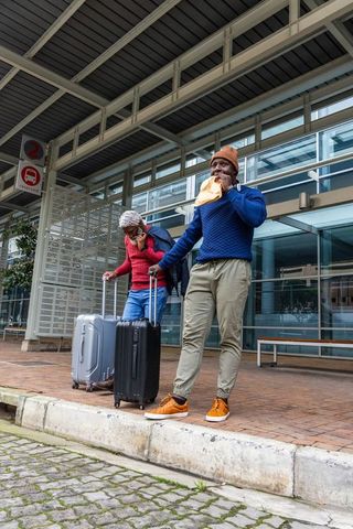 African american travelers waiting at transit canopy with luggage and mobile phones