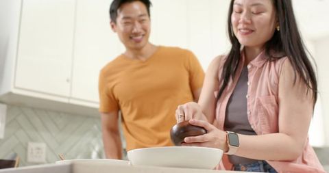 Diverse couple prepping meal in modern kitchen with woman grinding spice over bowl
