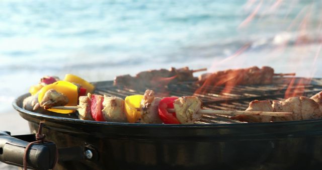 Colorful kebabs with pieces of meat and bell peppers grilling on barbecue beside ocean at sunset. Ideal for depicting summer vacations, outdoor activities, travel destinations, or promotion of culinary events and recipes.