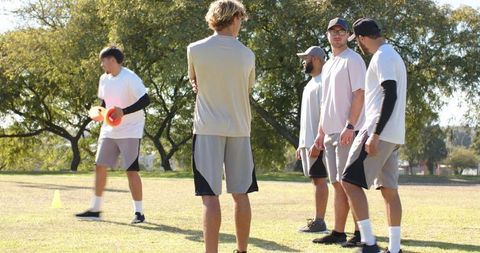 Diverse male teammates practicing outdoor cone drills on sunny park field