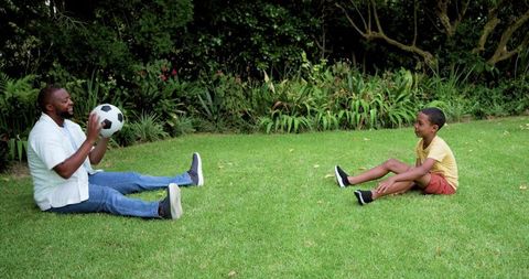 Father coaching son playing soccer on backyard lawn, practicing passing drills and bonding