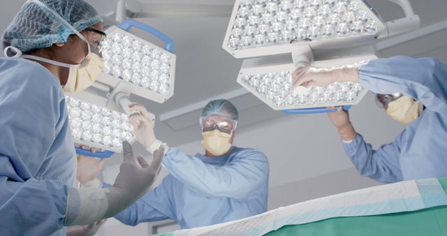 Surgeons wearing masks and gloves are adjusting surgical lights while preparing for a surgery in an operating room. This image is suitable for use in healthcare publications, promotional materials for hospitals or medical services, and educational content regarding surgical procedures and medical training.