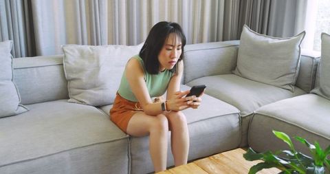 Asian Woman Engaged with Smartphone in Minimalist Living Room