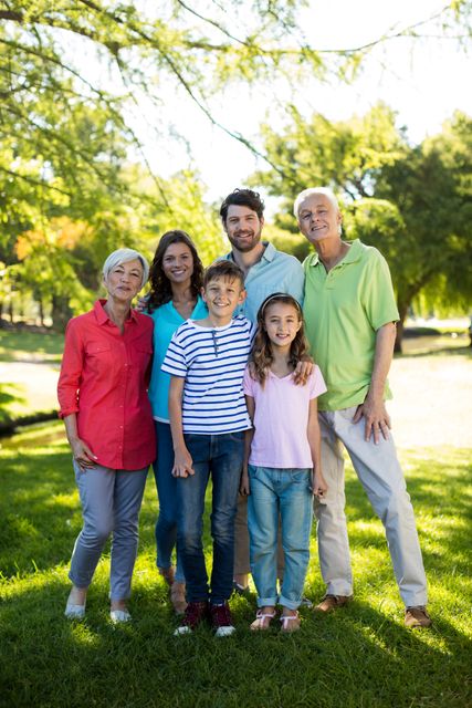 Multigenerational family smiling and posing together in a park on a sunny day. Ideal for use in advertisements, family-oriented content, health and wellness promotions, and community-focused campaigns.