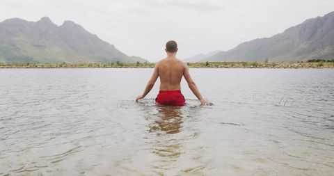 Solitary man wading in mountain lake waters reflecting tranquility
