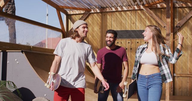 Group of three friends enjoying sunny day at skatepark. Two holding skateboards, walking, and smiling, showing joy and casual conversation. Ideal for portraying youth culture, active lifestyles, outdoor fun, social gatherings, and the spirit of friendship.