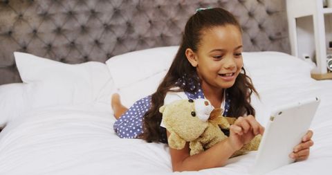 Smiling Girl Engaged with Tablet on Cozy Bed