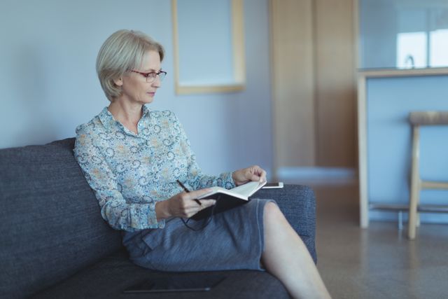 Businesswoman reading book while sitting on sofa in office