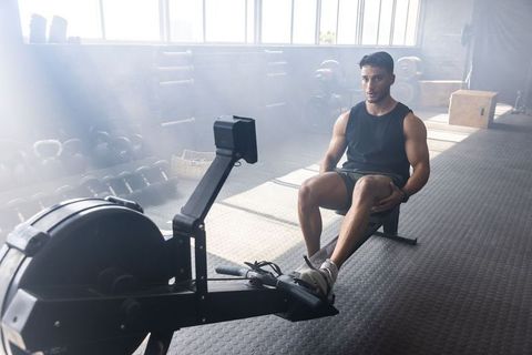 Middle Eastern man rowing on indoor rower in sunlit gym, strength training focus