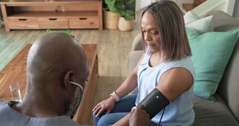 Caregiver measuring blood pressure with arm cuff during at-home wellness visit on couch