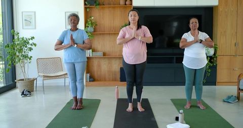 Senior african american women practicing mindful yoga together on mats in sunlit living room