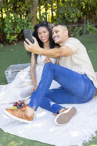 Couple taking selfie on picnic blanket in backyard enjoying casual outdoor romance