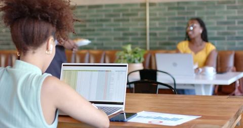 Young woman working on spreadsheet in coffeehouse coworking space with laptop