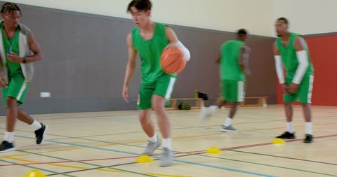 Asian male basketball player dribbling through cones during indoor team training drills