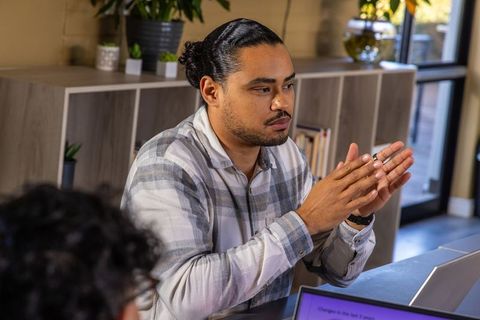Discussing strategy with focused colleague gesturing while working on laptop in office