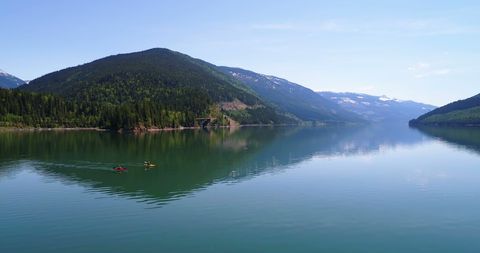 Kayakers enjoy a serene paddle on a calm mountain lake, with copy space. The tranquil waters and surrounding forested hills create a perfect setting for outdoor recreation and relaxation.