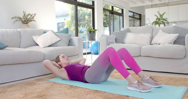 Woman performs exercise on yoga mat in cozy and bright living room with modern decor. Ideal for use in promotions for home workout programs, fitness articles, health and wellness blogs, or advertisements for athletic apparel.