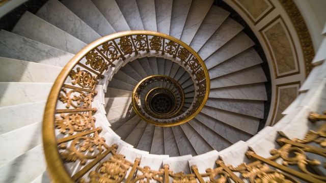 Spiraling marble staircase revealing gilded balustrade and ornate central medallion