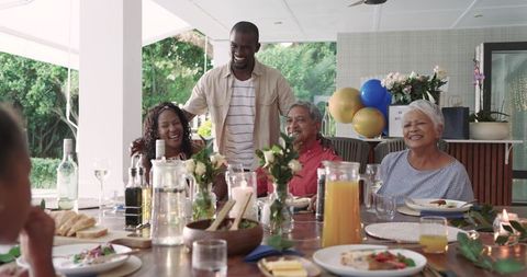 Multigenerational Family Celebrating Dinner on Covered Patio with Balloons and Flowers