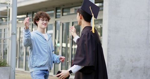 Friends celebrating graduate in cap and gown on campus embracing after commencement