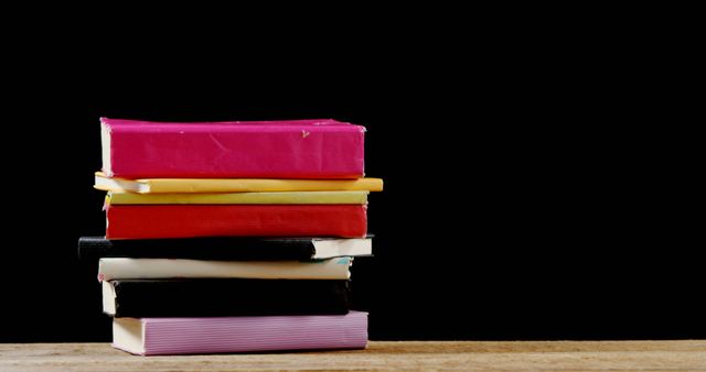 Stack of brightly colored books on a wooden surface against a black background. Ideal for themes related to education, reading, studying, literature, and knowledge. Can be used in blogs, articles, websites, and educational materials.