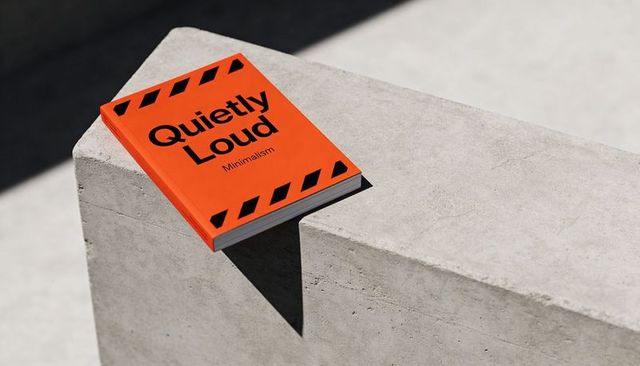 Bright orange paperback resting on concrete plinth casting sharp shadow, minimalist