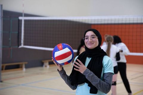 Young muslim woman in hijab holding volleyball during indoor team practice, smiling athlete
