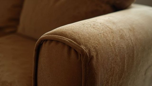Close-up showing brown velvet sofa armrest highlighting seam, stitching and fabric texture