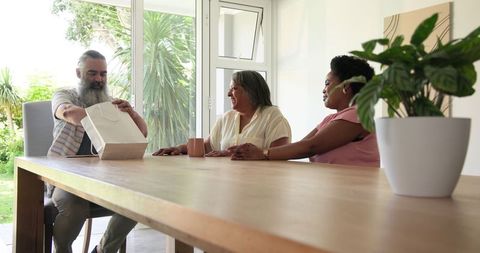 Senior Man Shares Gift with Smiling Women at Home Celebration