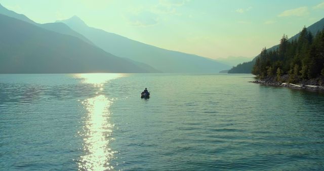 A lone boat navigates through the tranquil waters of a mountainous lake at sunset, with copy space. The serene landscape and golden light create a peaceful and picturesque setting for outdoor activities.