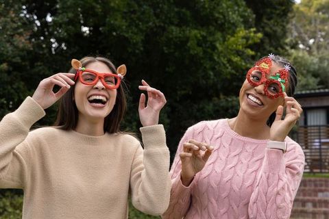 Friends laughing wearing festive novelty glasses outdoors in cozy sweaters