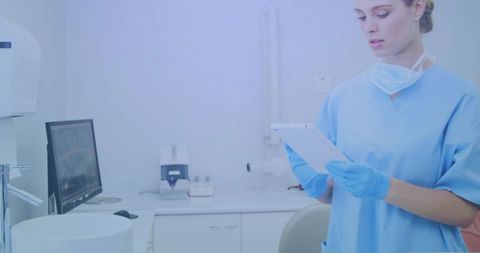 Dental hygienist reviewing tablet in sterile treatment room wearing scrubs gloves mask
