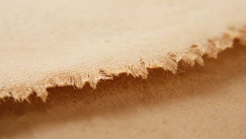 Fraying beige fibrous sheet revealing torn edge macro texture for design backgrounds