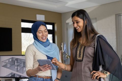 Muslim women coworkers reviewing tablet and pointing at architectural plan on monitor