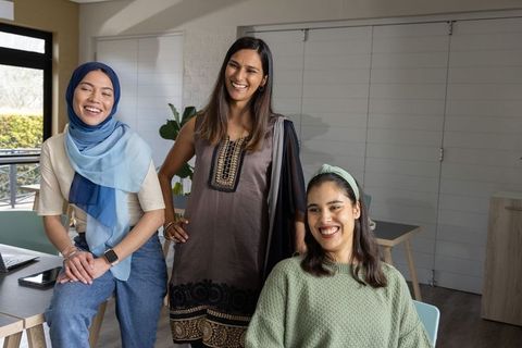 Diverse women laughing and collaborating in coworking lounge with laptop showcasing teamwork