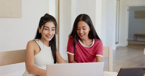 Smiling young women collaborating on laptops in modern home workspace