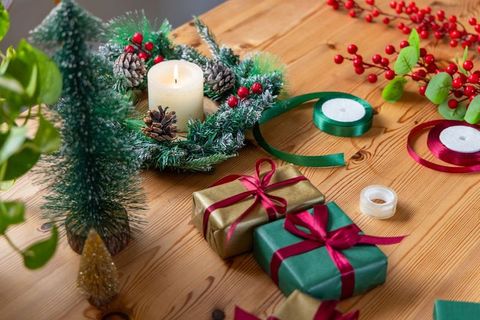 Wrapping holiday gifts on wooden table with candle wreath, ribbons and pinecones