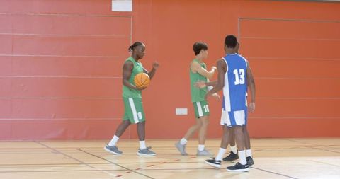 African american player dribbling, teammates defending and assisting in indoor basketball