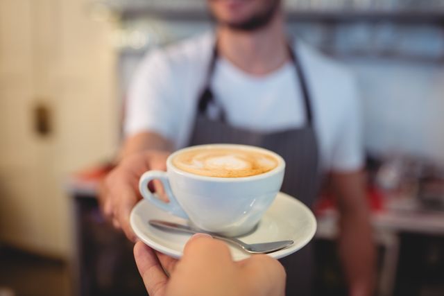 This image depicts a customer receiving a cup of coffee from a waiter at a cafe. The focus is on the interaction between the customer and the waiter, highlighting the service and hospitality aspect of the cafe experience. This image can be used for promoting coffee shops, illustrating customer service, or in articles about cafe culture.