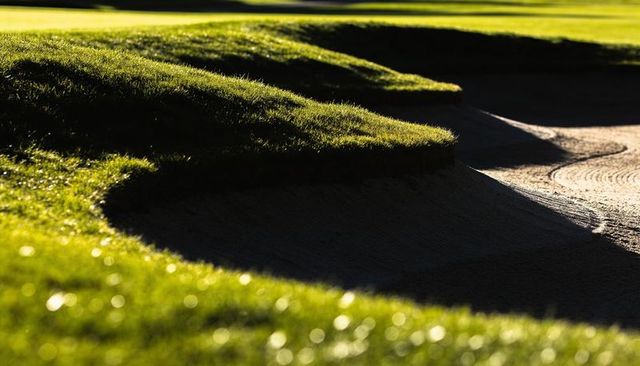 Highlighting low-angle sunlit bunker lips and sculpted grass contours on golf fairway