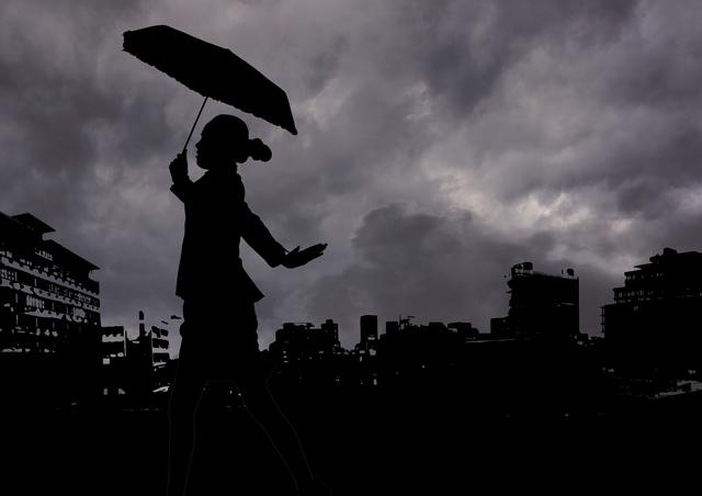 Silhouette of woman holding umbrella walking against stormy clouds and cityscape