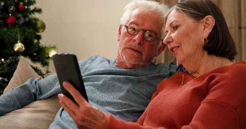 Senior Couple Sharing Tablet on Sofa with Christmas Tree in Background
