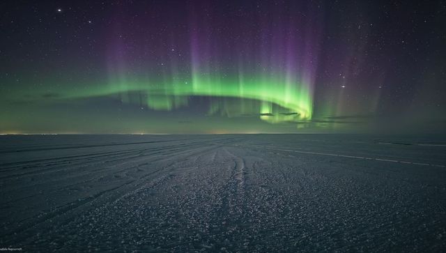 Aurora dancing over frozen arctic plain with snowmobile tracks under starry purple sky