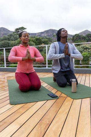 African american couple practicing outdoor meditation on terrace with mountain view