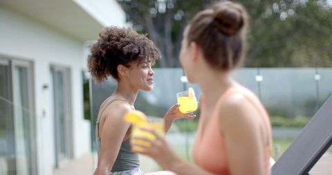 Diverse friends chatting and sipping citrus cocktails on modern patio by glass railing
